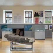 Exhibition in the West Kerry Museum, in the centre is an Ogham stone. The background features a series of exhibition panels covering topics ragngins from gaelic football to the medieval period.
